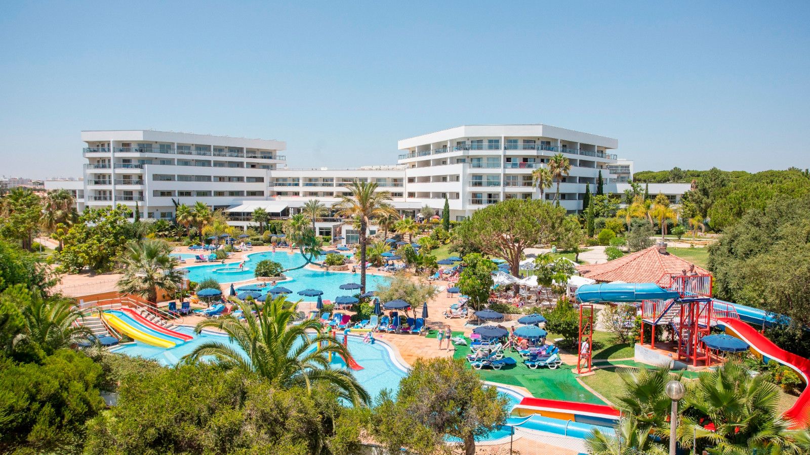 Overview of the vibrant pool area at Alfagar I Village, featuring multiple pools, water slides, and sun loungers, perfect for family fun and relaxation.